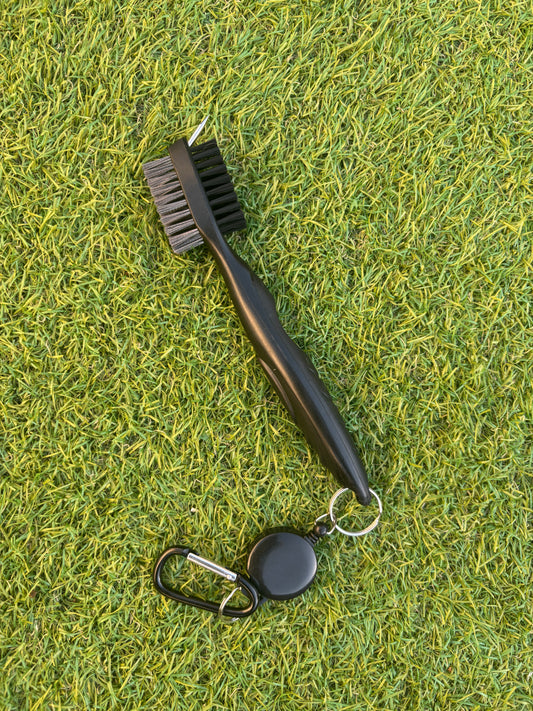 Black 4-in-1 golf club cleaning brush with retractable clip on green grass background