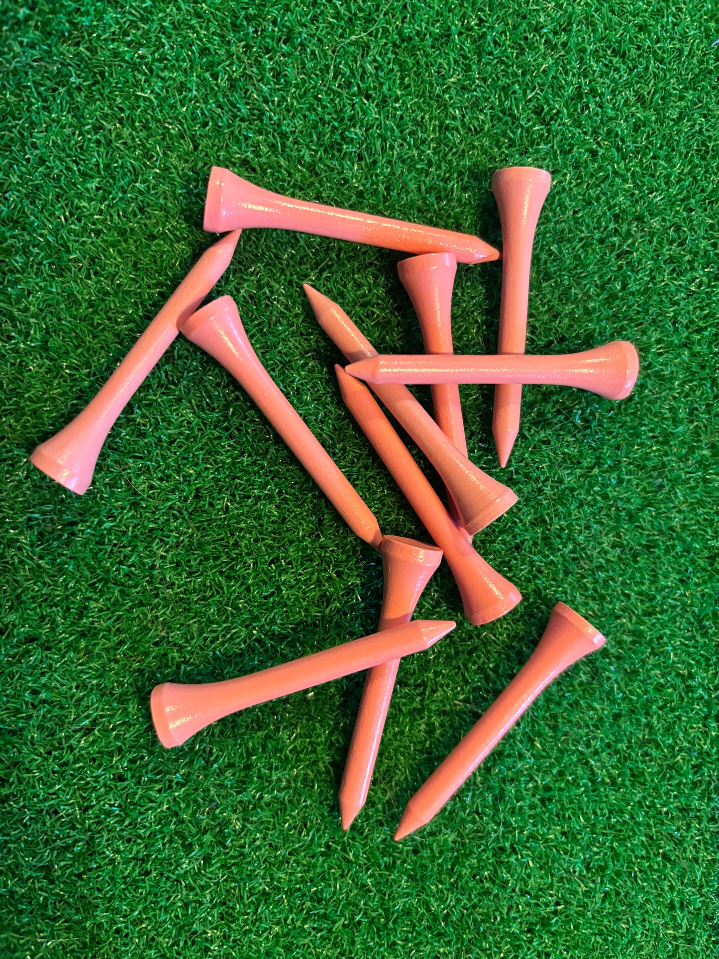 Pink 54mm golf tees on a green grass background