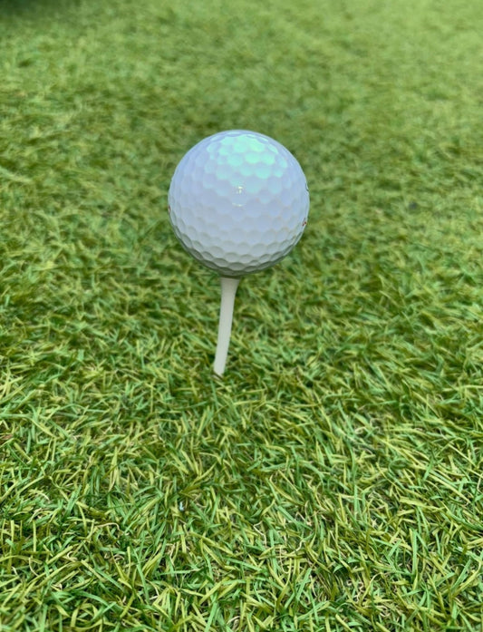 white 70mm golf tee with a golf ball on top in a golf tee box with a grass background