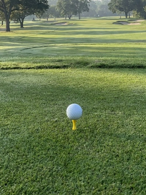 Yellow castle tee with a golf ball on top with a golf course in the background 