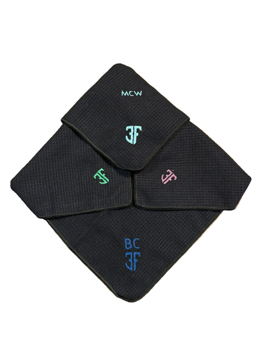 4 personalised embroidered black waffle towels with blue green and pink lettering on a white background